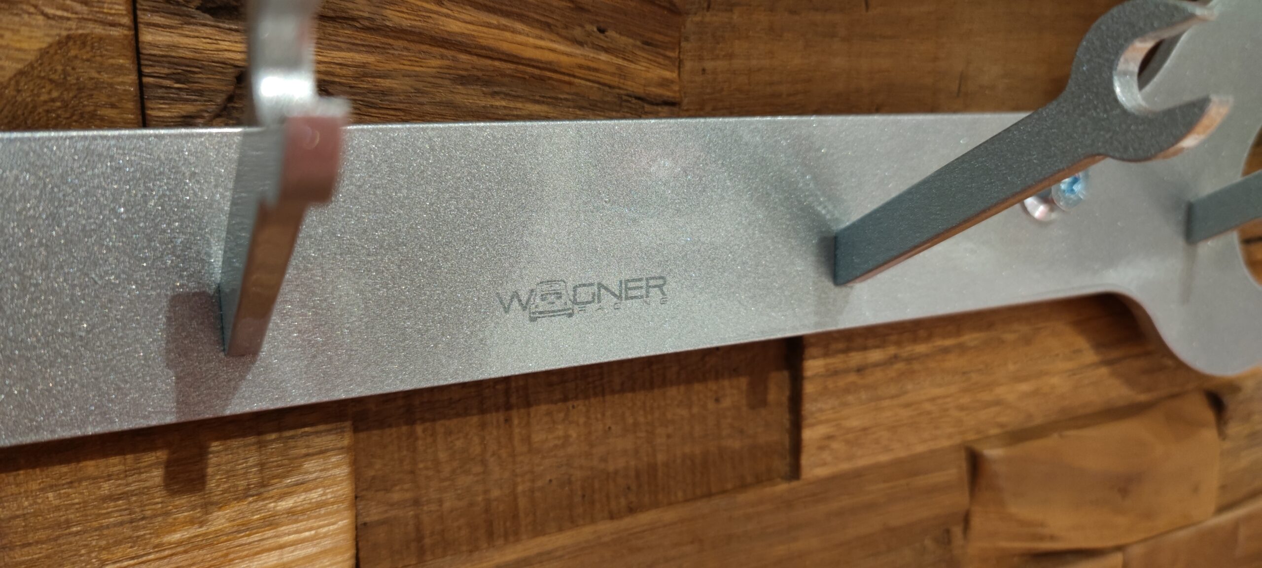 Detailaufnahme der silbernen Schraubenschlüssel-Garderobe mit Kleiderhaken und Wagner-Racing-Logo.